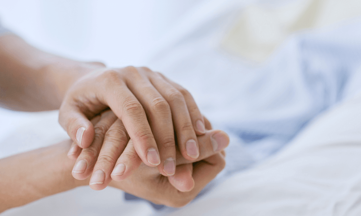 Two hands clasped in care on a soft white sheet