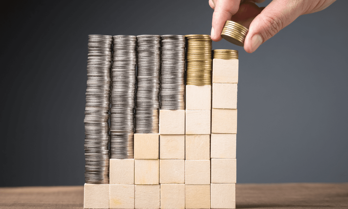 A hand placing a coin on stacked coins and wooden blocks forming a staircase
